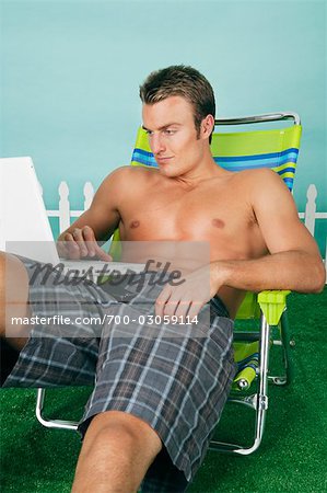 Homme assis dans la chaise de jardin à l'aide d'ordinateur portable