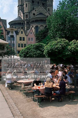 People sitting at an outdoors restaurant near St. Martin church which rises above the Fish Market in the old town, Cologne, North Rhine Westphalia, Germany, Europe
