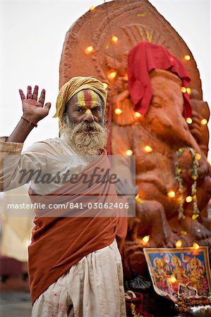 Holy man raises a hand in front of a Ganesh statue draped in fairy lights at the Hindu festival of Shivaratri, Pashupatinath, Kathmandu, Nepal, Asia