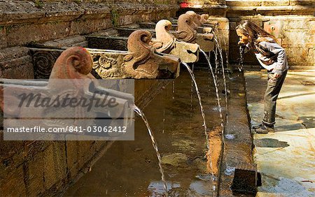 Mädchen nimmt einen Drink von der Wasserspeier in einem Tempel-Hof am Godavari im Süden von dem Kathmandu-Tal, Nepal, Asien