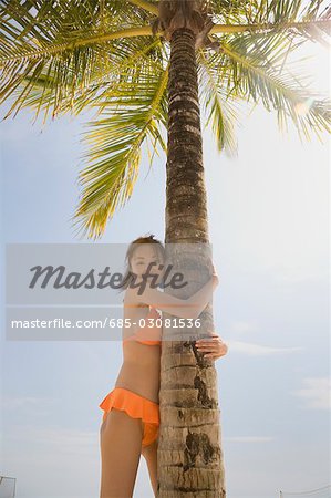 Young woman in bikini holding palm tree