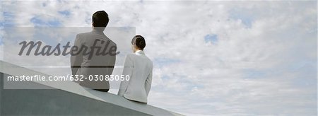 Homme d'affaires et femme d'affaires assis côte à côte sur le rebord de toit
