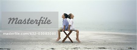Deux garçons assis dos à dos sur chaise sur la plage