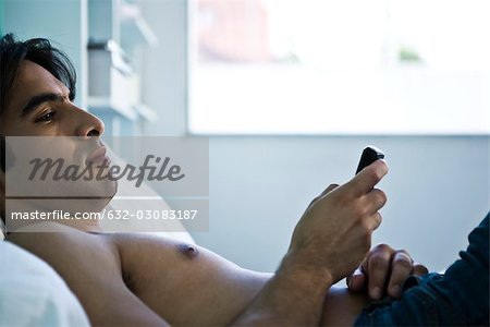 Man reclining on bed looking at cell phone