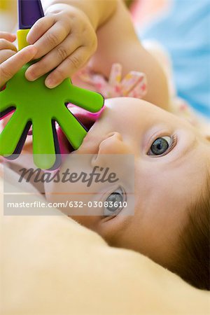 Bébé fille à mâcher sur les jouets en plastique, regardant la caméra