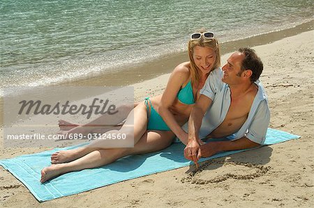 Couple allongé sur la plage, il peint un coeur dans le sable