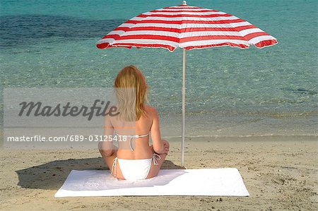 Woman sitting on the beach under a sunshade - back view