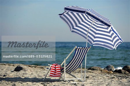 Blaue und weiße Sonnenschirm und Liegestuhl am Strand