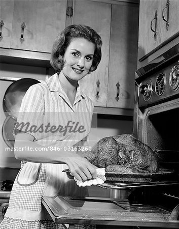 1960s SMILING HOUSEWIFE REMOVING THANKSGIVING ROAST TURKEY FROM OVEN