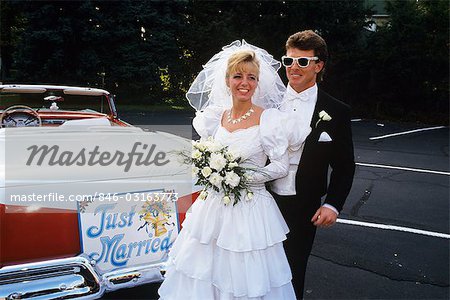 1991 BRIDE AND GROOM STANDING NEXT TO VINTAGE CONVERTIBLE FORD CAR
