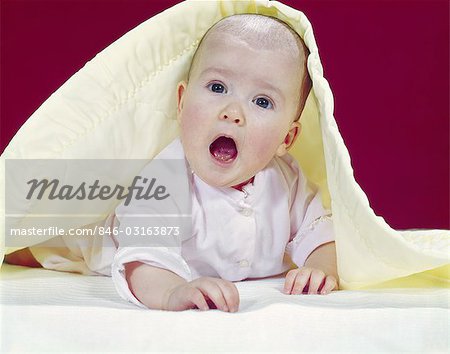 1960s BABY MOUTH WIDE OPEN PEEKING OUT FROM UNDER YELLOW BLANKET SURPRISED FACIAL EXPRESSION