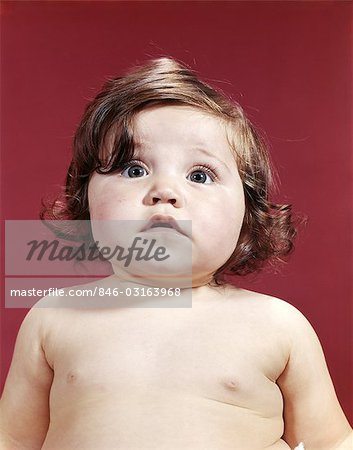 1960s PORTRAIT BRUNETTE BABY GIRL WITH CHUBBY ROUND FACE UNCERTAIN FACIAL EXPRESSION