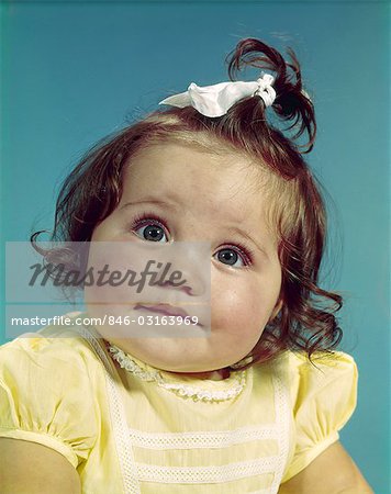 1960s BRUNETTE BABY GIRL ROUND CHUBBY FACE YELLOW DRESS RIBBON TOPKNOT INTERESTED SINCERE FACIAL EXPRESSION