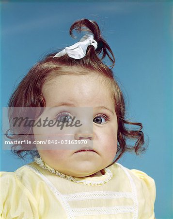 1960s BRUNETTE BABY GIRL RIBBON TOPKNOT YELLOW SHIRT CHUBBY CHEEKS ROUND FACE SAD UNHAPPY FACIAL EXPRESSION