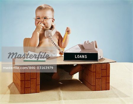 1960s BABY BUSINESSMAN DIAPER SITTING AT TOY DESK LOANS BANK SIGN WEARING EYEGLASSES TALKING ON TELEPHONE