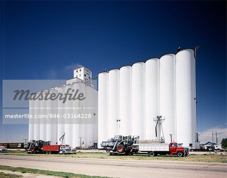 1970ER JAHRE WEIßE KORN AUFZÜGE LKW GEPARKT VOR SILOS GEGEN BLAUEN HIMMEL