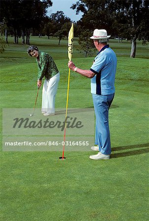 1980s SENIOR COUPLE PLAYING GOLF WOMAN PUTTING ON GREEN