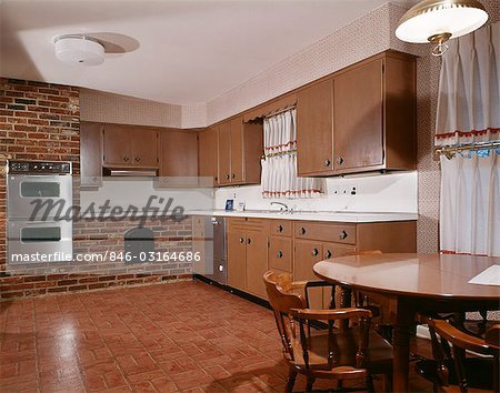 1970s KITCHEN WITH DARK WOODEN CABINETS BRICK WALL AND DOUBLE OVEN