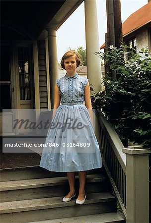 1950s TEENAGE GIRL IN BLUE DRESS STANDING ON PORCH STAIRS