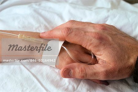 ADULT HAND HOLDING CHILD'S HAND ON HOSPITAL BED