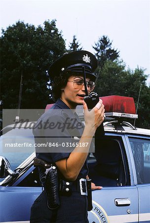 1970s POLICE WOMAN TALKS ON WALKIE-TALKIE BY POLICE CAR