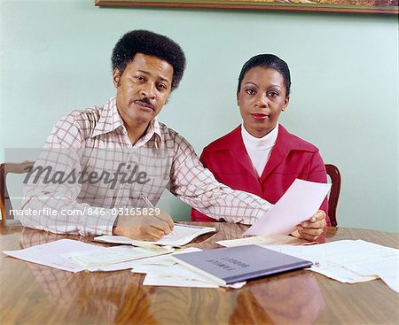 MILIEU DES ANNÉES 70 ANS AFRO-AMÉRICAIN COUPLE HOMME FEMME ASSISE À TABLE EN PASSANT PAR LES COMPTES DE MÉNAGE