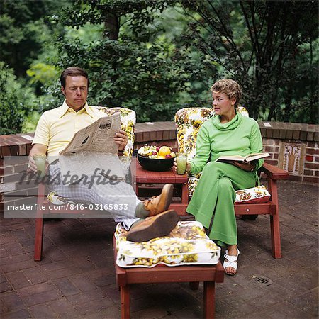 1970s COUPLE MAN WOMAN MIDDLE AGED SITTING PATIO DECK READING BOOK NEWSPAPER