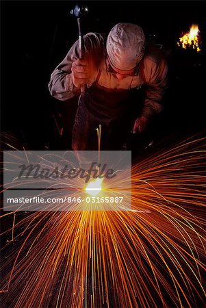 BLACKSMITH WORKING WHITE HOT IRON WITH A HAMMER RED AND ORANGE SPARKS FLYING IN ALL DIRECTIONS