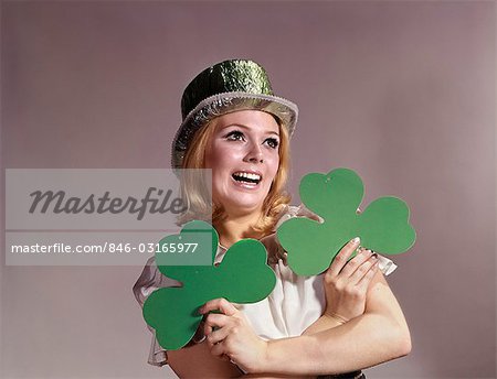 1960s WOMAN SMILING HOLDING GREEN SHAMROCKS WEARING GREEN PARTY HAT FOR SAINT PATRICK'S DAY