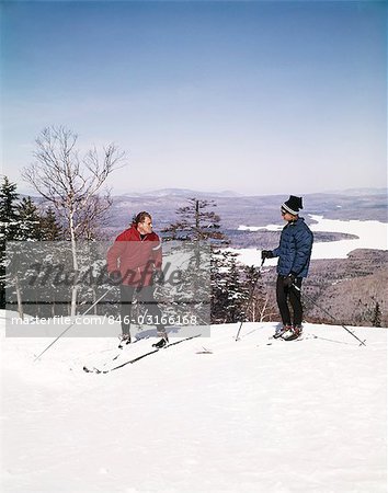 1960s COUPLE MAN WOMAN SKIERS TOP HILL