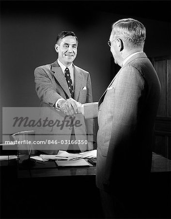 1950ER JAHRE MÄNNER SCHÜTTELN HÄNDE ANZÜGE DESK BUSINESS PAPIERKRAM