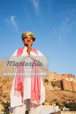 Man in prayer position with fort in the background, Meherangarh Fort, Jodhpur, Rajasthan, India