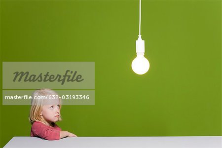 Little girl biting lip looking with concern up at illuminated light bulb suspended overhead