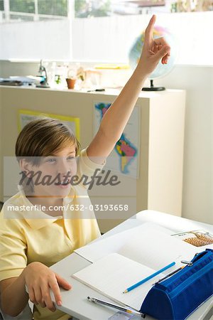 Boy sitting in classroom, raising hand enthusiastically