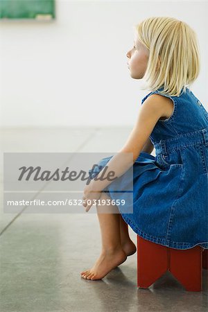 Little girl sitting on stool, looking away in thought