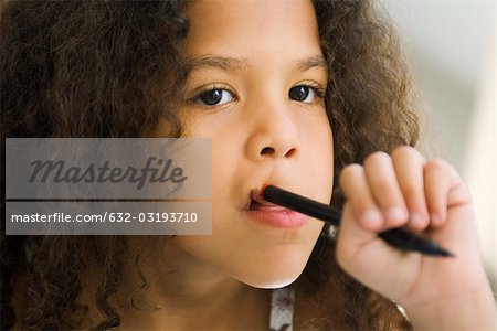 Little girl holding pen against mouth, looking away
