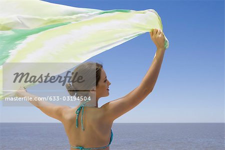 Young woman standing before sea, holding scarf in breeze