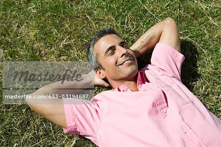 Homme couché sur l'herbe avec les mains derrière la tête et les yeux fermés, brin d'herbe dans la bouche