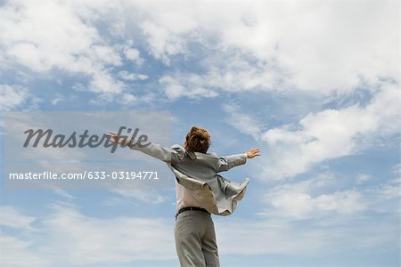 Homme d'affaires avec les bras tendus sur fond de ciel nuageux, vue arrière