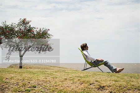 Man relaxing in lounge chair outdoors contemplating sea shore view