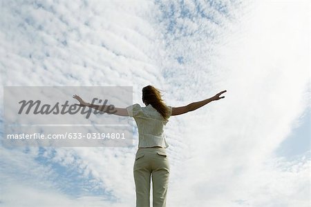 Woman with arms outstretched, cloudy sky in background, rear view