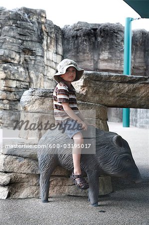 Junge sitzt auf der Statue von Wildschwein