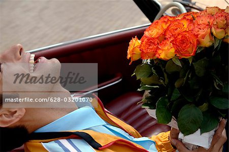 Junger Mann mit schwarzen Haaren sitzen in einem Auto mit einem Strauß Rosen, Nahaufnahme