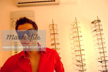 Jeune homme avec des cheveux noir Lunettes de soleil grand dans un magasin plein de lunettes, mise au point sélective