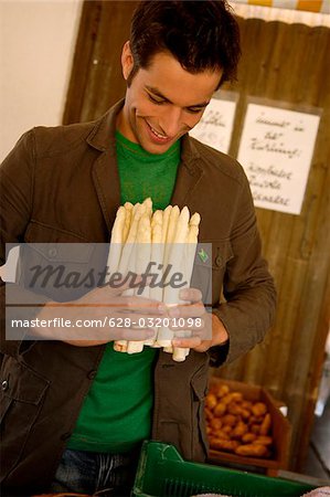Young man with black hair holding a bunch of asparagus in his hands, selective focus