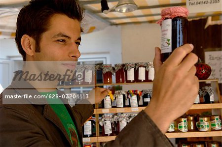 Jeune homme aux cheveux noirs examinant un verre préserver avec de la confiture, mise au point sélective