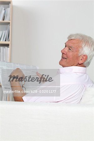 Senior homme lisant journal sur canapé
