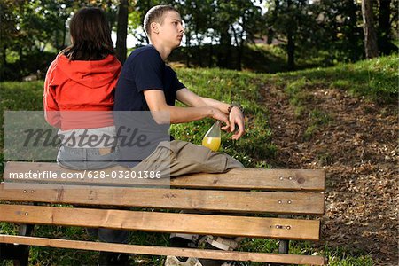 Teenager couple sitting on a back of a bench and looking in different directions