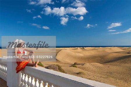 Woman sitting on a fence looking at the sand dunes, Maspalomas, Gran Canaria, Spain