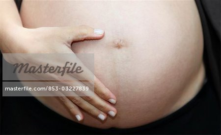 Pregnant woman holding her belly, close-up, front view